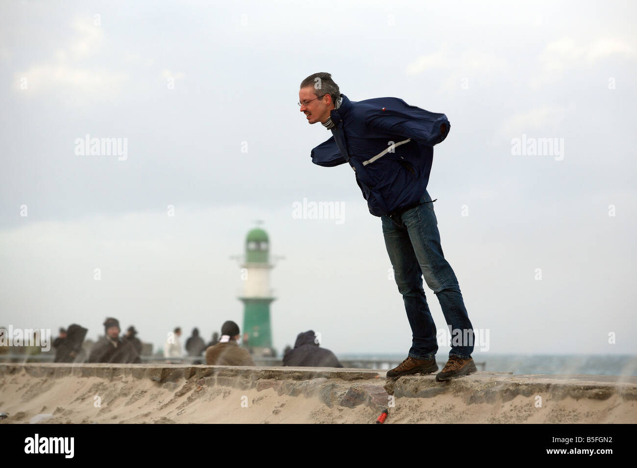 Man lehnte sich gegen den stürmischen Wind auf einem westlichen Wellenbrecher, Warnemünde, Deutschland Stockfoto