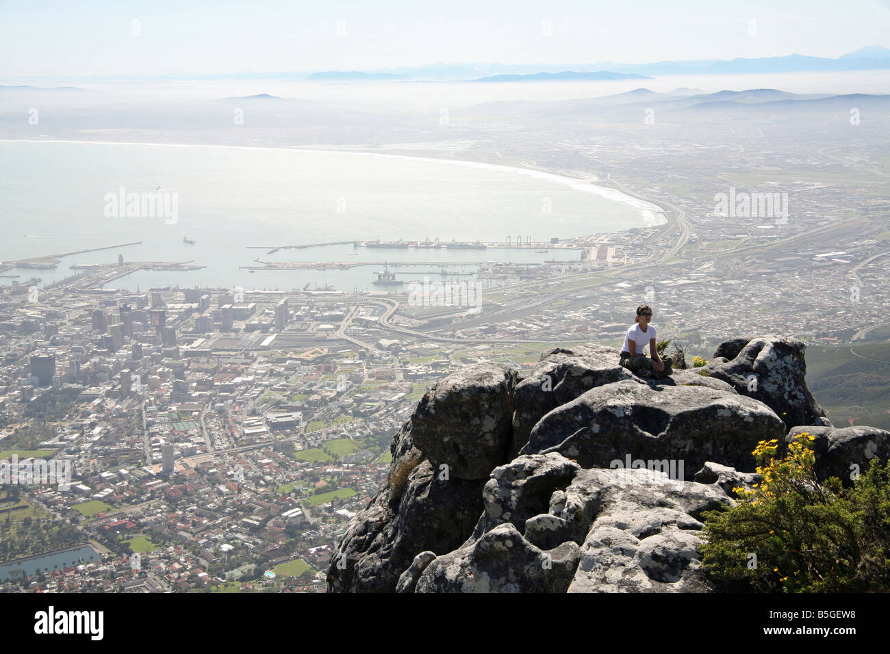 Eine junge Frau sitzt auf der Oberseite Tafelberg mit Blick auf die City of Cape Town in Südafrika. Stockfoto