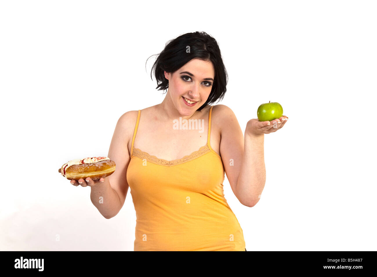 Eine junge Frau versucht, zwischen einem gesunden Apfel und eine ungesunde Donut entscheiden. Stockfoto