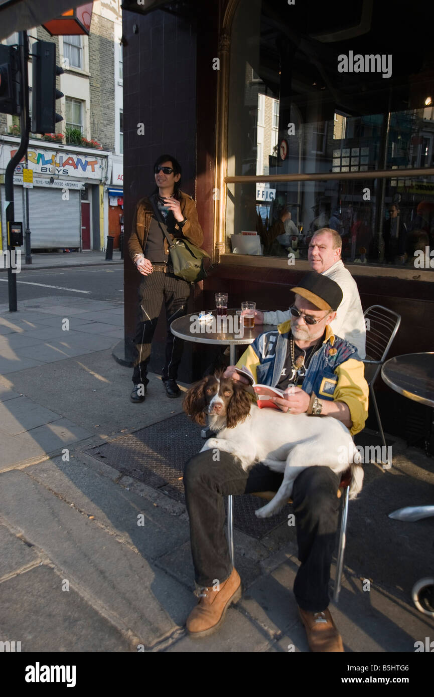 Ein Mann sitzt mit einem Hund auf dem Schoß einen Drink vor dem Warwick Castle Pub in Portobello Nottinghill West London Stockfoto