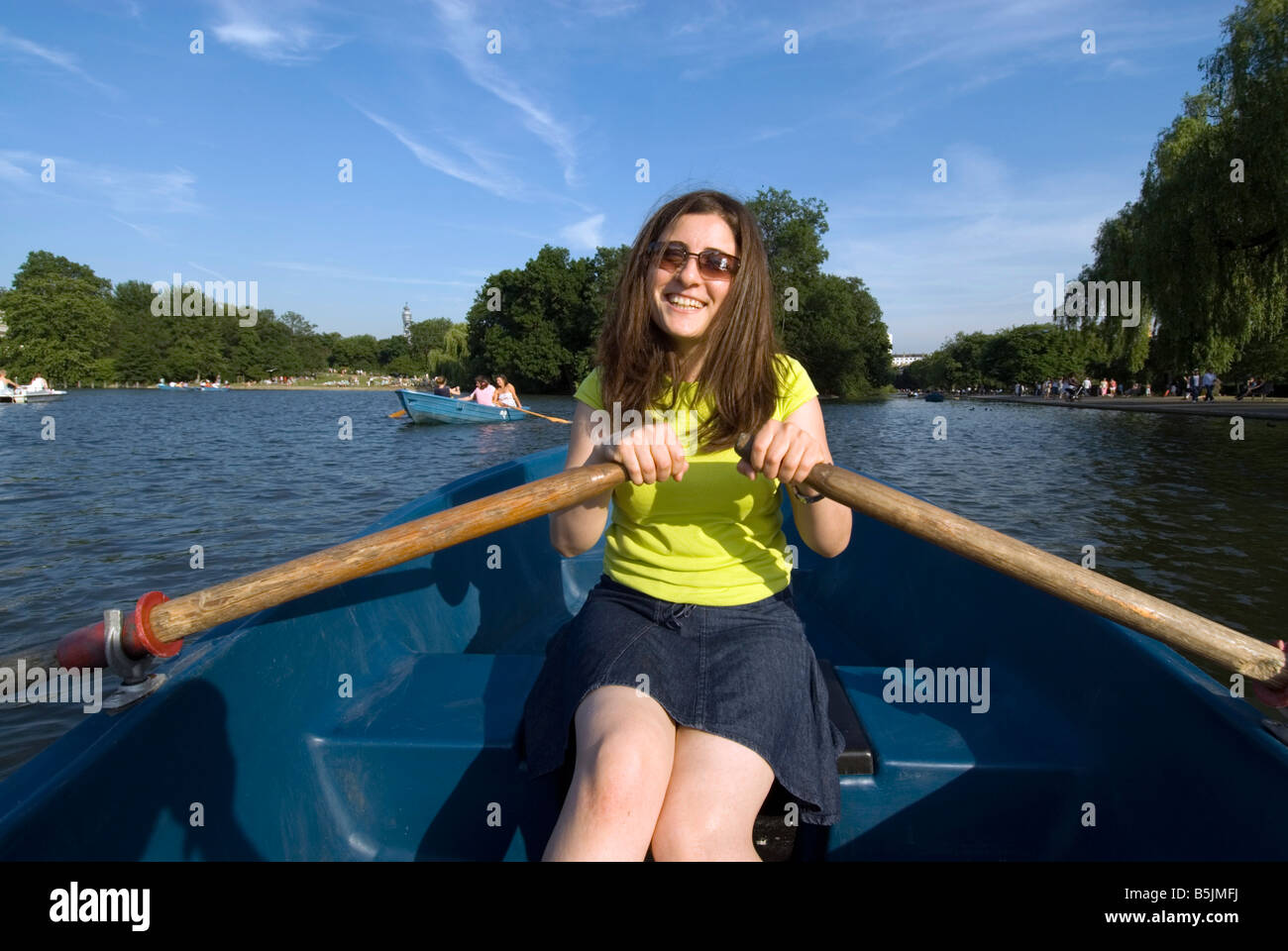 Junge Frau Rudern auf dem See mit Booten im Regents Park, London, England UK Stockfoto