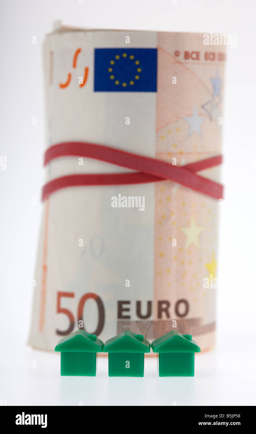 drei grüne Häuser vor der ein Bündel von 50 Euro-Banknoten Bargeld gefesselt in einer Rolle mit Gummizug Stockfoto