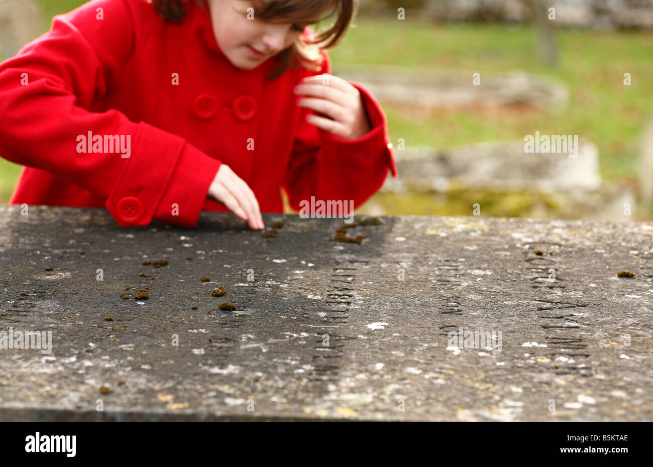 Ein zehn Jahre altes Mädchen untersuchen die Legende auf einem alten Grab. Stockfoto