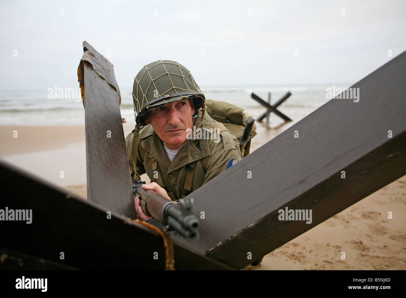 Ein Schauspieler verkleidet als ein amerikanischer Soldat d-Day an Omaha Beach Normandie Frankreich hinter einer "Igel" Tank-Falle. Stockfoto