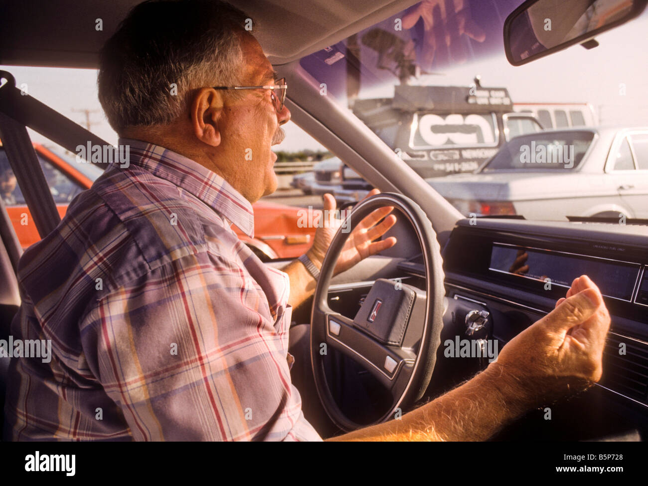 Verärgerter senior Mann hinter Rad des Autos Gesten und schreit ein anderer Fahrer. Stockfoto