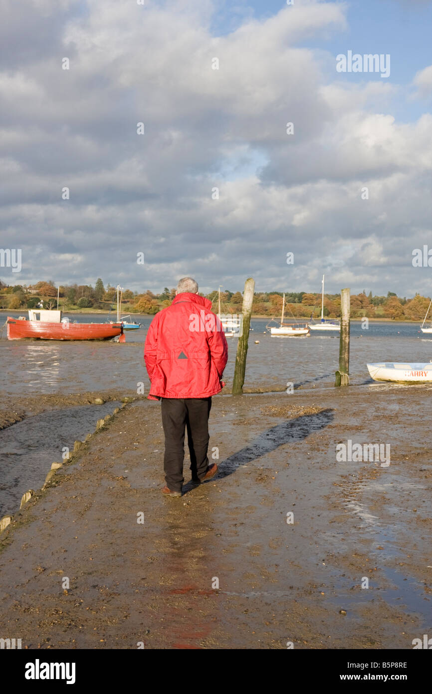 Ein Mann in einem roten Mantel sieht jenseits des Flusses Orwell von Pin Mill schwer Suffolk Stockfoto