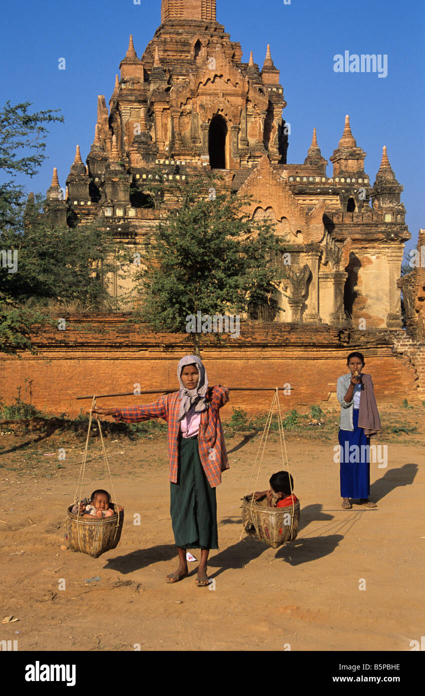 Eine burmesische Frau trägt ihre beiden Kinder in Körben vor dem Tayok Pye Tempel in Bagan, Burma bzw. Myanmar Stockfoto