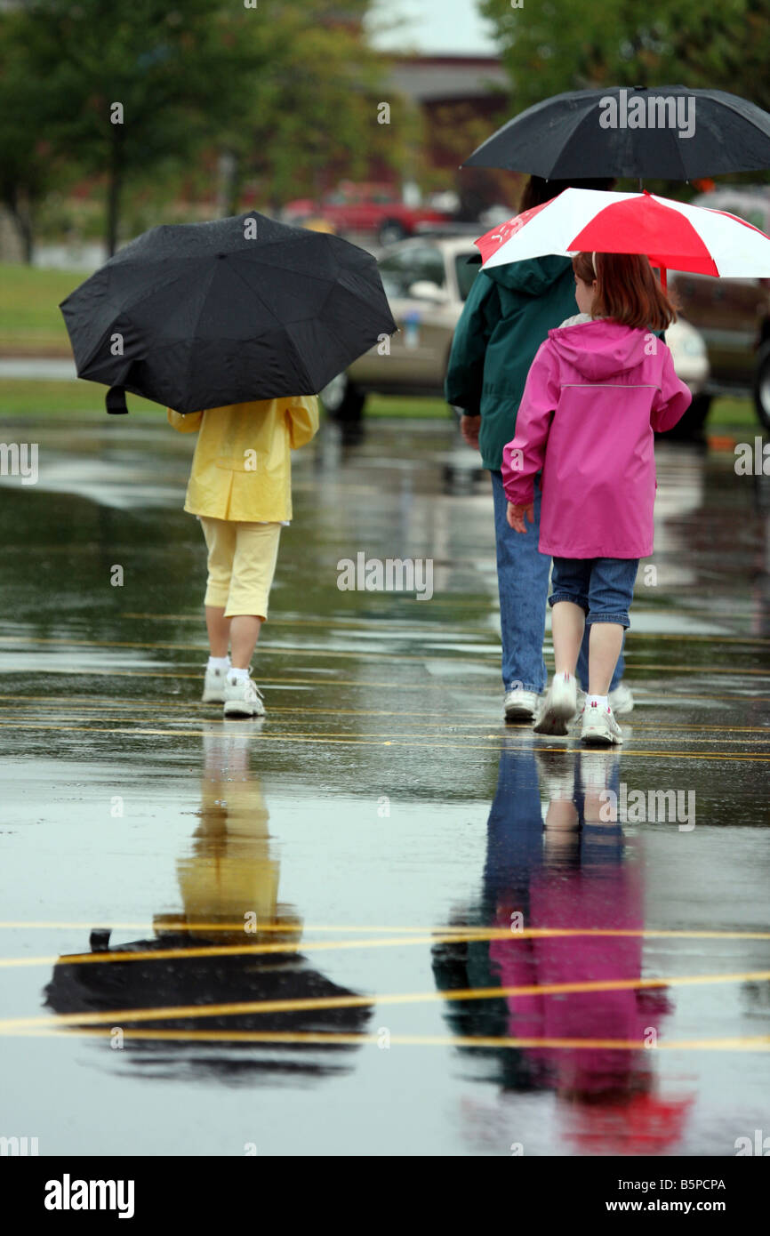 Mutter und zwei Kinder zu Fuß mit Sonnenschirmen im Regen auf einem Feuer Sicherheit Messe Stockfoto
