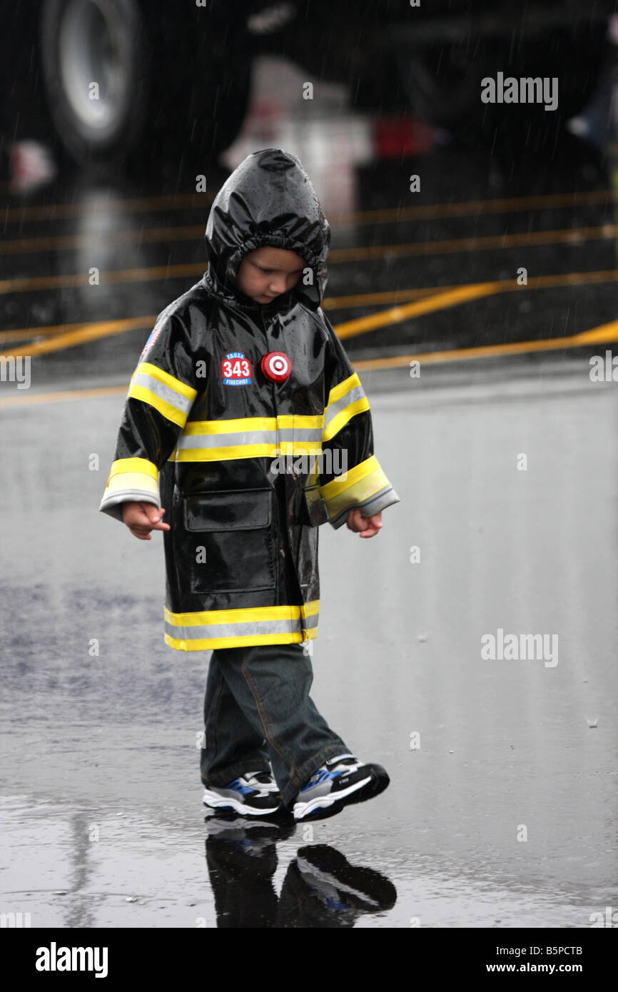 Ein kleiner Junge, Wandern in den Regen in seinen Feuerwehrchef Regenjacke während ein Feuer-Sicherheit-Messe Stockfoto