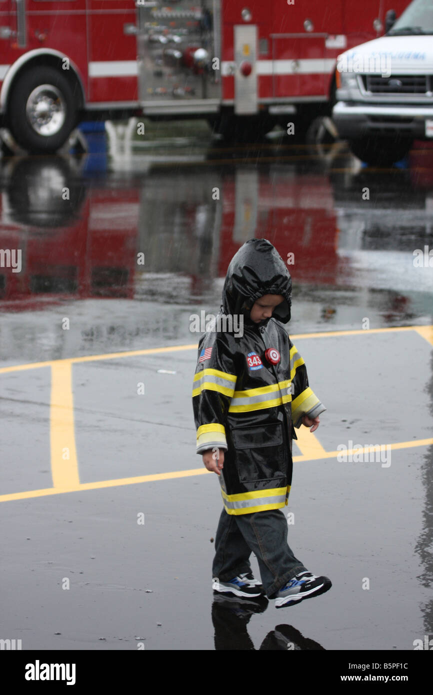 Ein kleiner Junge, Wandern in den Regen in seinen Feuerwehrchef Regenjacke während ein Feuer-Sicherheit-Messe Stockfoto