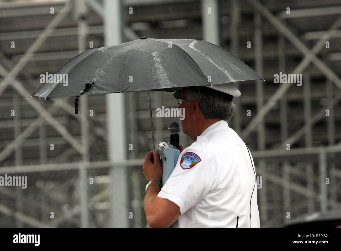 Der MC-Feuerwehrmann sprechen über ein Mikrofon an der Masse unter einem Regenschirm im Regen auf einem Feuer Sicherheit Messe Stockfoto