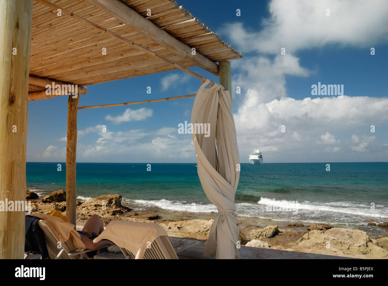 Ein Reisender lounges in einer Hütte am Strand von Little Stirrup Cay.  Kreuzfahrtschiff, die Majestät der Meere in der Ferne gesehen werden kann. Stockfoto