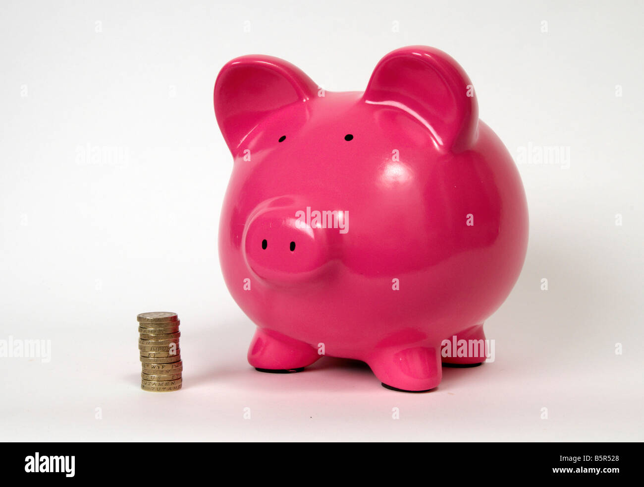 halbe Seitenprofil einer rosa Piggy Bank mit einem Haufen oder Stapel von Pfund-Münzen sitzen davor auf einem weißen wieder Boden. Stockfoto