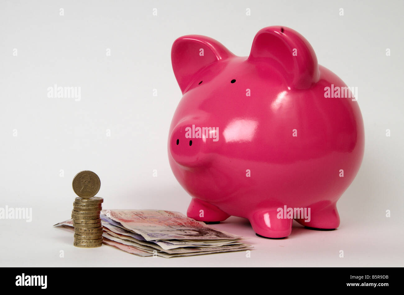 eine halbe Seitenprofil ein rosa Schweinchen bank mit einem Haufen von Münzen und britische Banknoten vor es Stockfoto