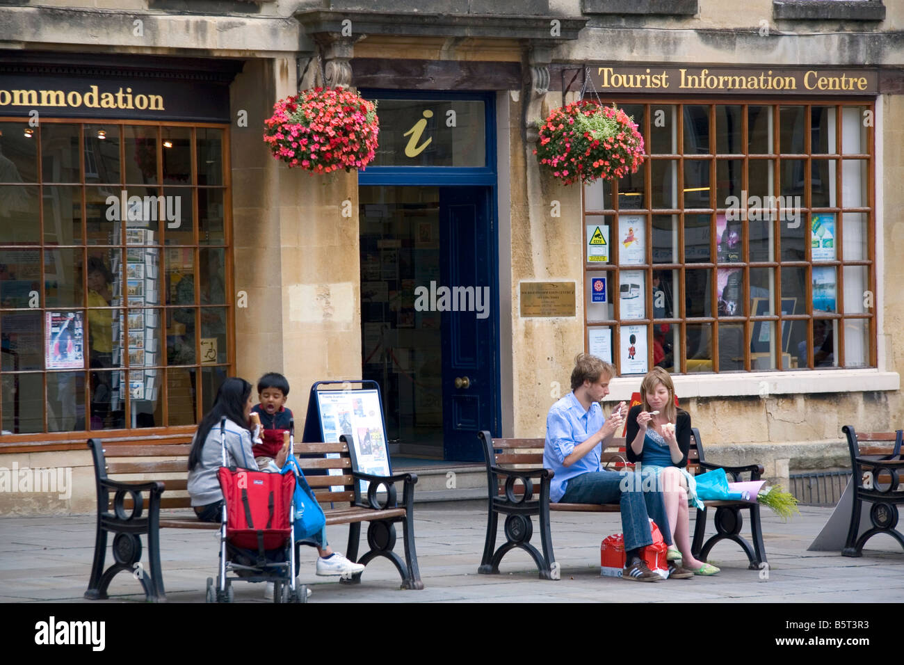 Menschen essen Eis auf Parkbänken vor der Tourist Information Centre in Bath, Somerset, England Stockfoto