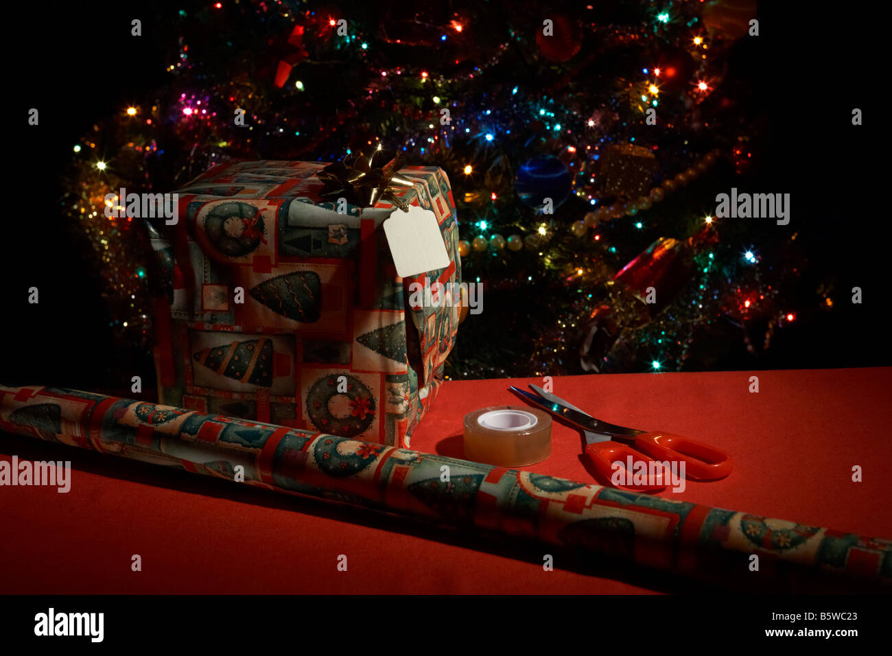 verpackte Weihnachtsgeschenk mit Packpapier Papier-Klebeband und Schere vor Weihnachtsbaum Stockfoto