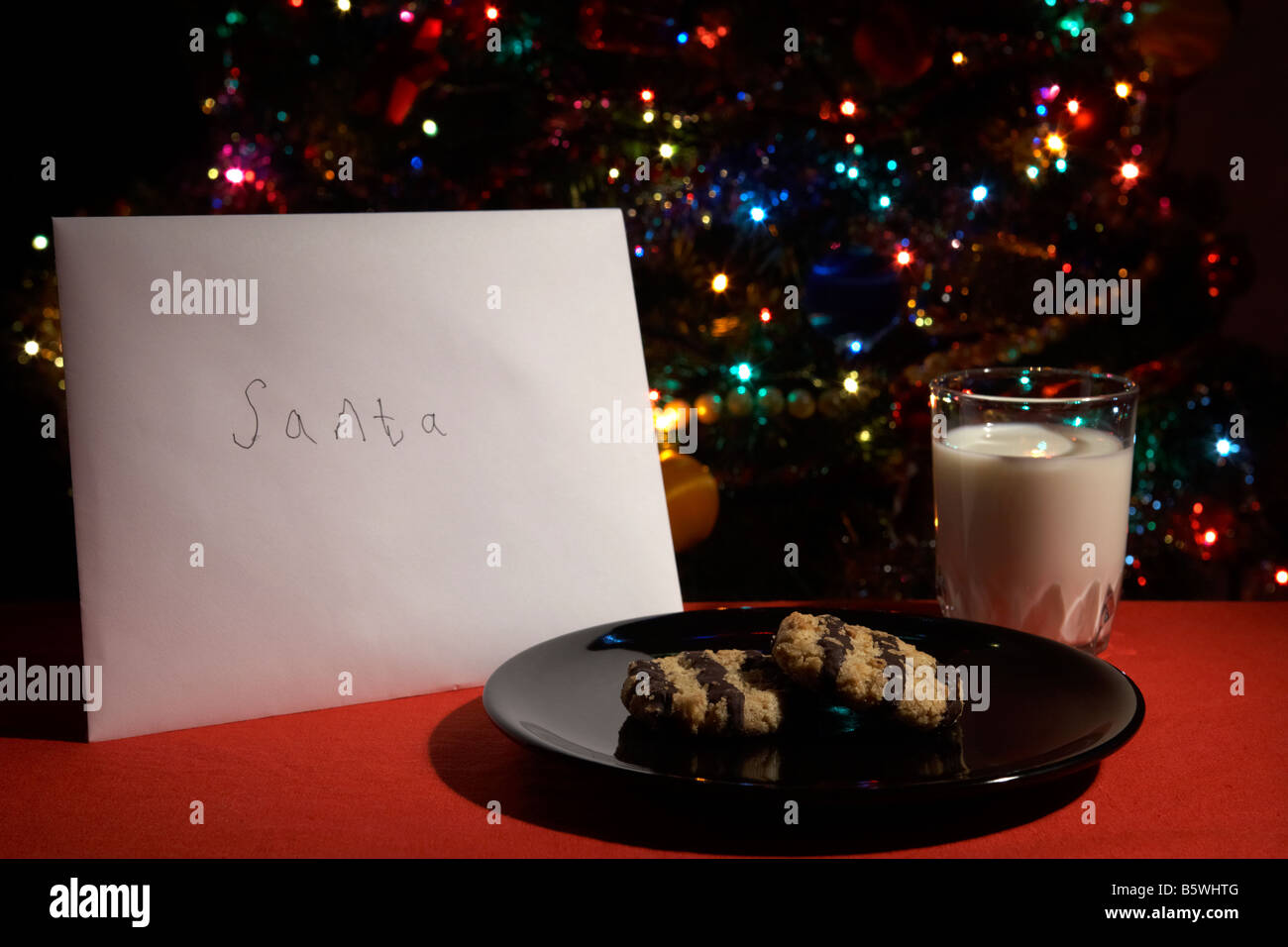 Kinder-Brief an den Weihnachtsmann ausgelassen am Heiligabend mit Keksen und Glas Milch vor dem Weihnachtsbaum Stockfoto