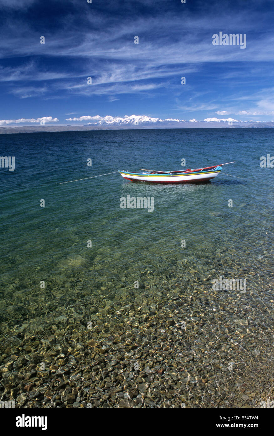 Fischerboot in klarem, flachem Wasser in der Nähe der Küste mit Sonnenlicht auf Kieselsteinen, Cordillera Real im Hintergrund, Mondinsel, Titicacasee, Bolivien Stockfoto