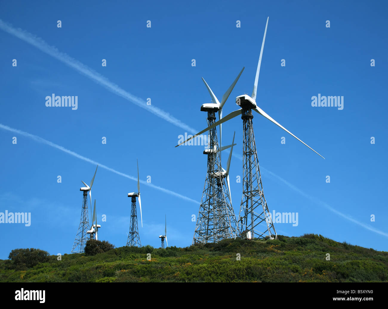 Moderne Windmühlen Turbine auf grünem Grund gegen blauen Himmel mit weißen Spuren der Jetliner Stockfoto