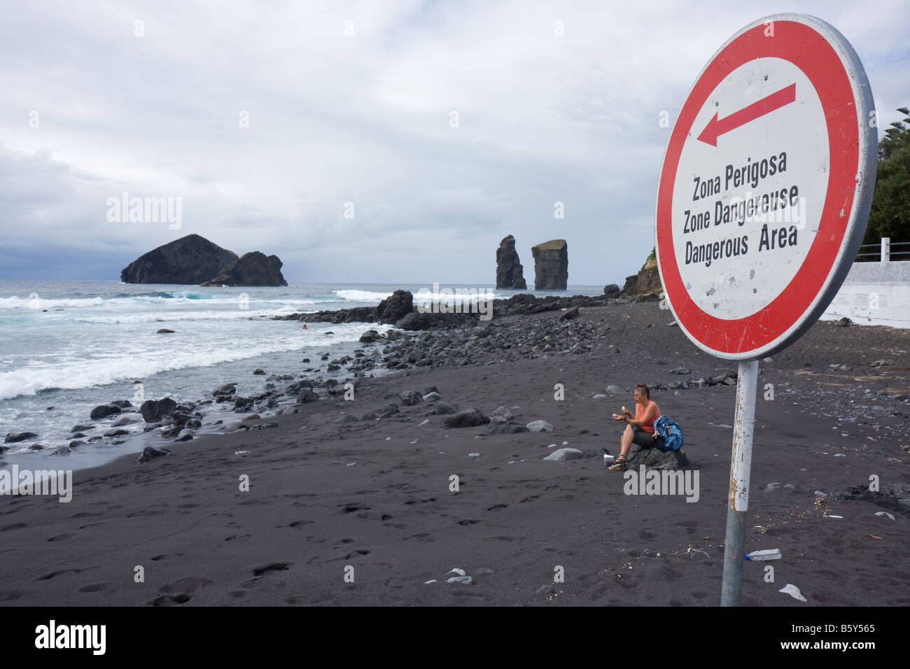 Frau sitzt auf einem Stein bei der schwarzen Lava-Sand am Strand von dem kleinen Dorf Mosteiros, Sao Miguel, Azoren Portugal Stockfoto