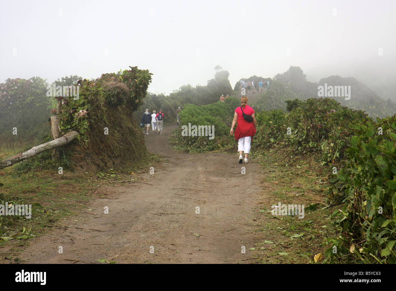 Touristen zu Fuß auf der schmalen Straße auf dem Kraterrand von Visto Rei, Richtung Westen, Sete Cidades, São Miguel, Azoren. Stockfoto