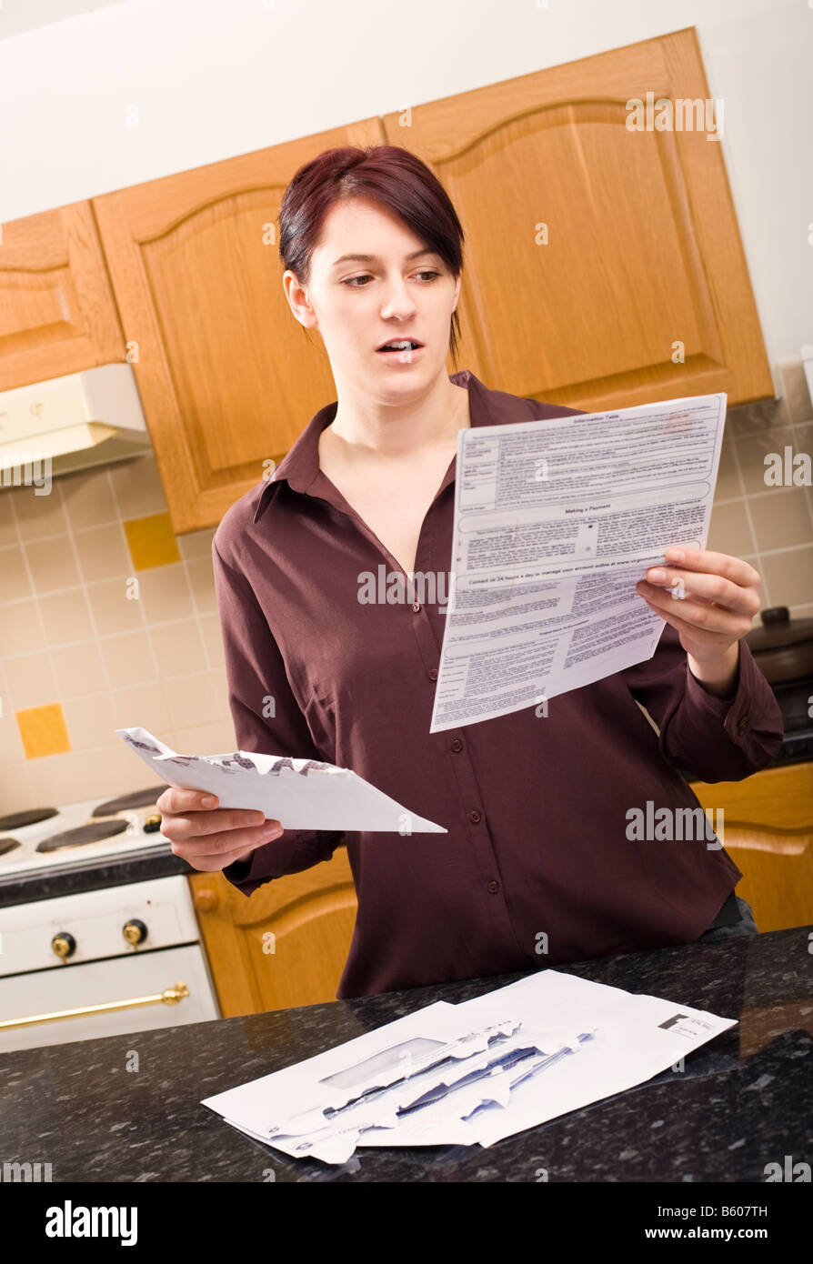 Junge Frau öffnet einen Brief und schaut unter Schock auf die Größe der Rechnung eingeschlossen Herr PR Stockfoto