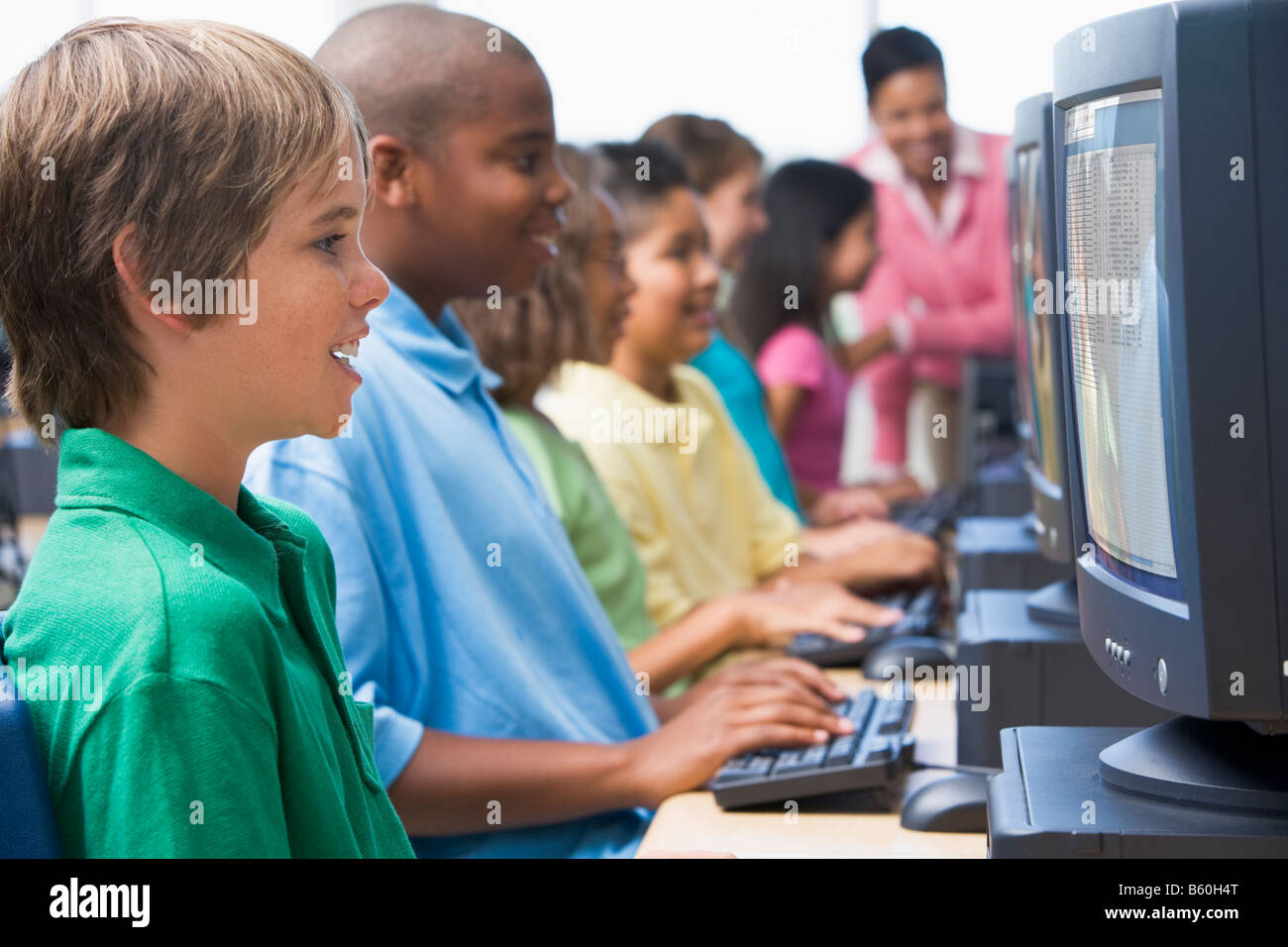 Sechs Kinder am Computer-Terminals mit Lehrer im Hintergrund (Schärfentiefe-Bereich/High-Key) Stockfoto