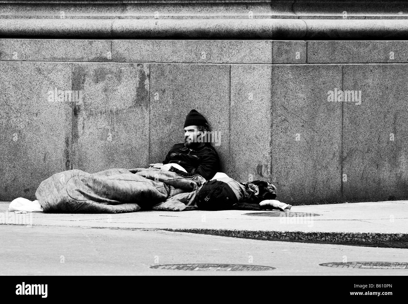 Ein schwarz-weiß Foto ein Obdachloser, ein Penner, ein Bettler, sitzen auf der Straße Ecke einer Straße in einer Großstadt. Stockfoto