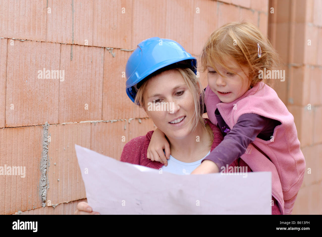 Mutter in einem blauen Schutzhelm und Tochter studiert die Pläne ihres Hauses auf der Baustelle Stockfoto