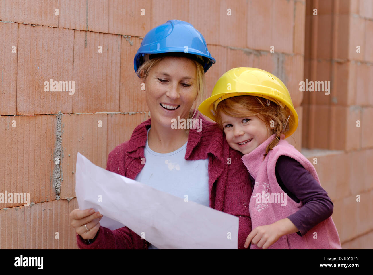 Mutter und Tochter tragen Schutzhelme und studiert die Pläne ihres Hauses auf der Baustelle Stockfoto