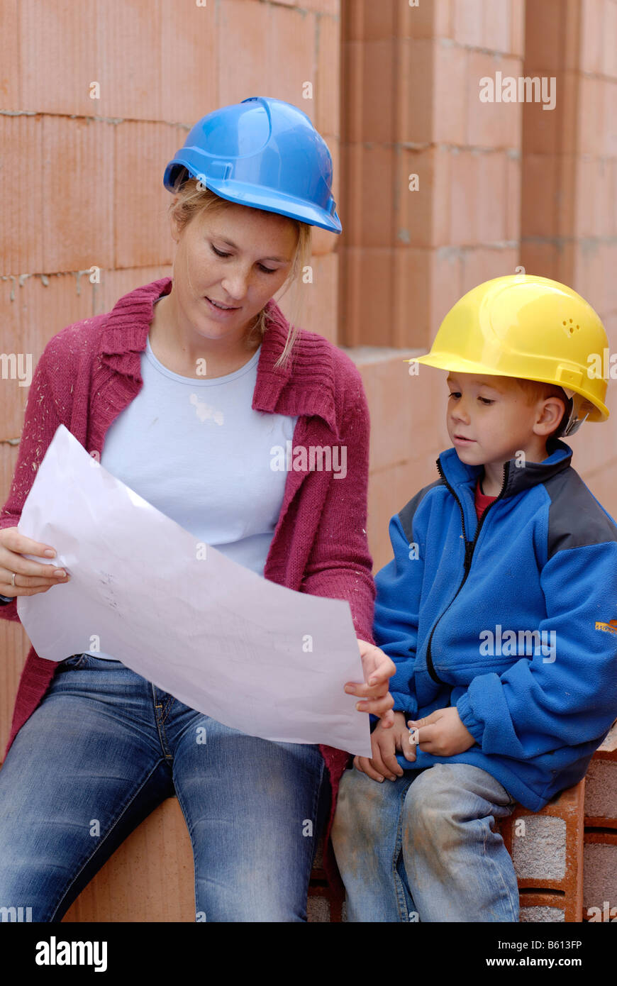 Mutter und Tochter tragen Schutzhelme und studiert die Pläne ihres Hauses auf der Baustelle Stockfoto