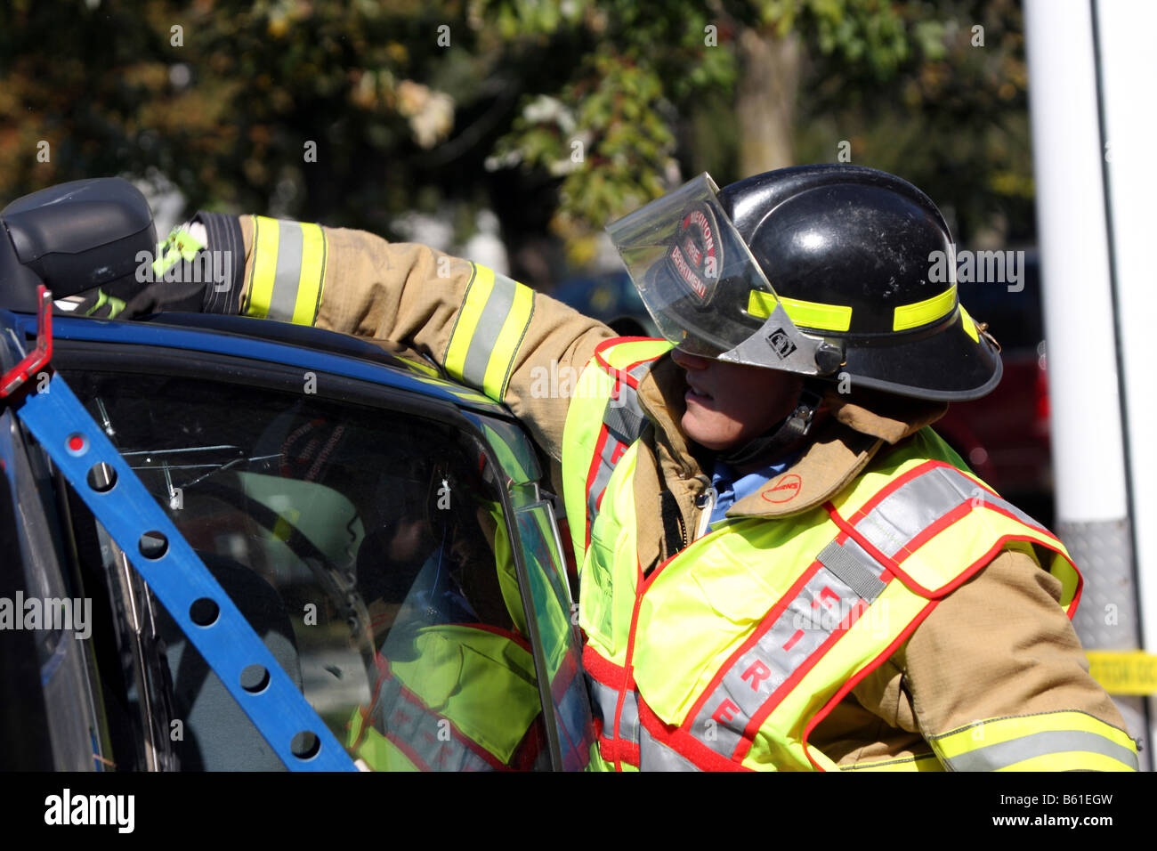 Die Fenster sind zerbrochen und die Feuerwehrmann ist Glas aus den Türrahmen eines stabilisierten rollovered Autos entfernen Stockfoto