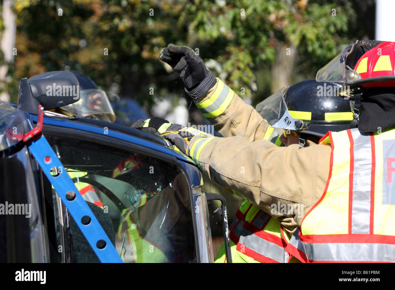Die Fenster sind zerbrochen und die Feuerwehrmann ist Glas aus den Türrahmen eines stabilisierten rollovered Autos entfernen Stockfoto