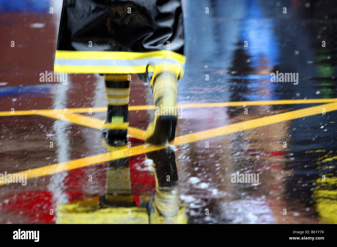 Einen künstlerischen Blick eines Kindes in eine schwarz-gelbe Feuerwehrmann Regenjacke im Regen auf nasser Fahrbahn Stockfoto