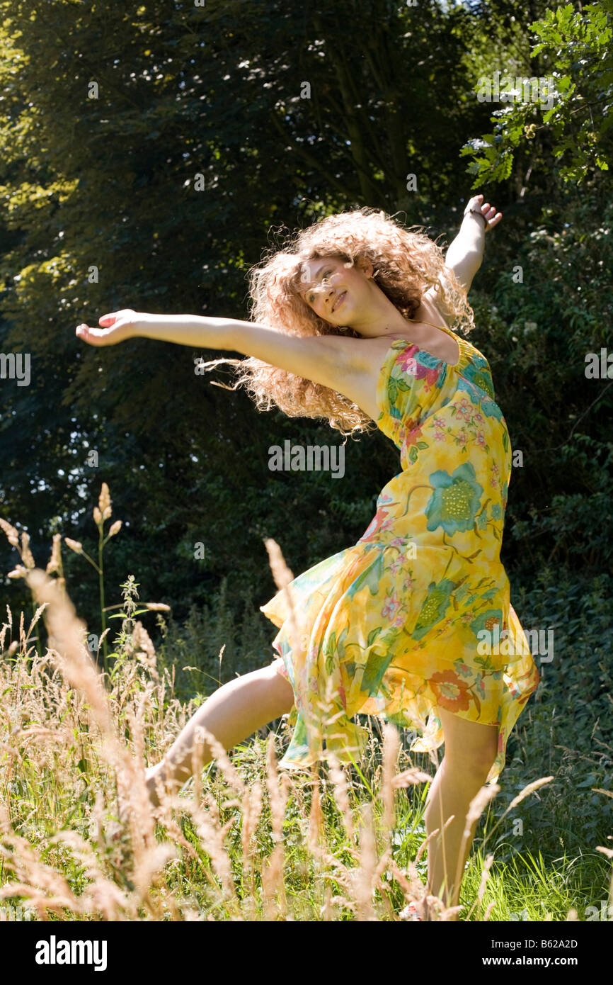 Junge Frau mit langen Haaren in einem gelben Kleid läuft über eine immer gewachsen Wiese Stockfoto