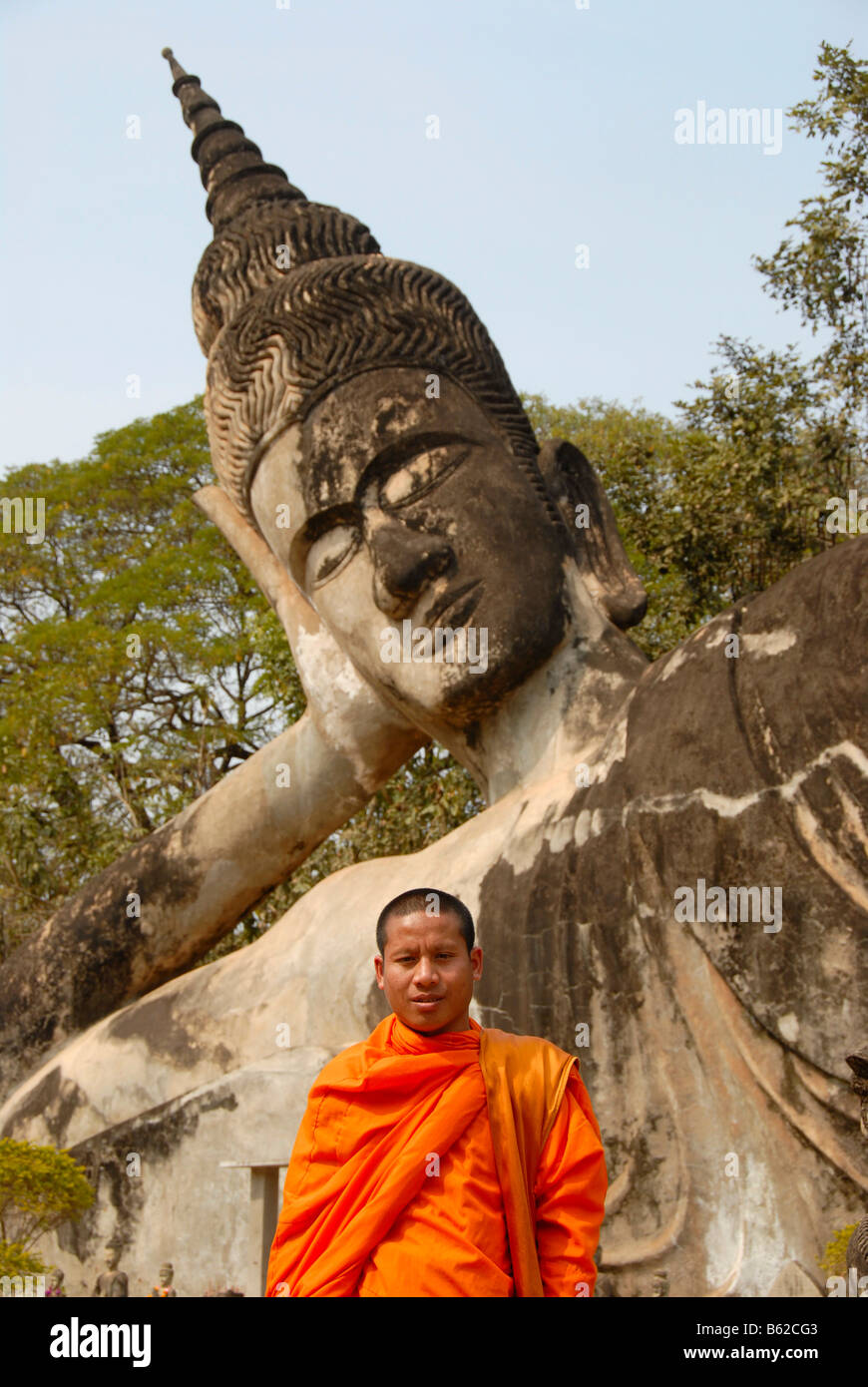 Buddhistischer Mönch trägt einen orangefarbenen Gewand vor einem liegenden Buddha Statue, Buddha Park, Suan Xieng Khuan, in der Nähe von Vientiane, Laos Stockfoto