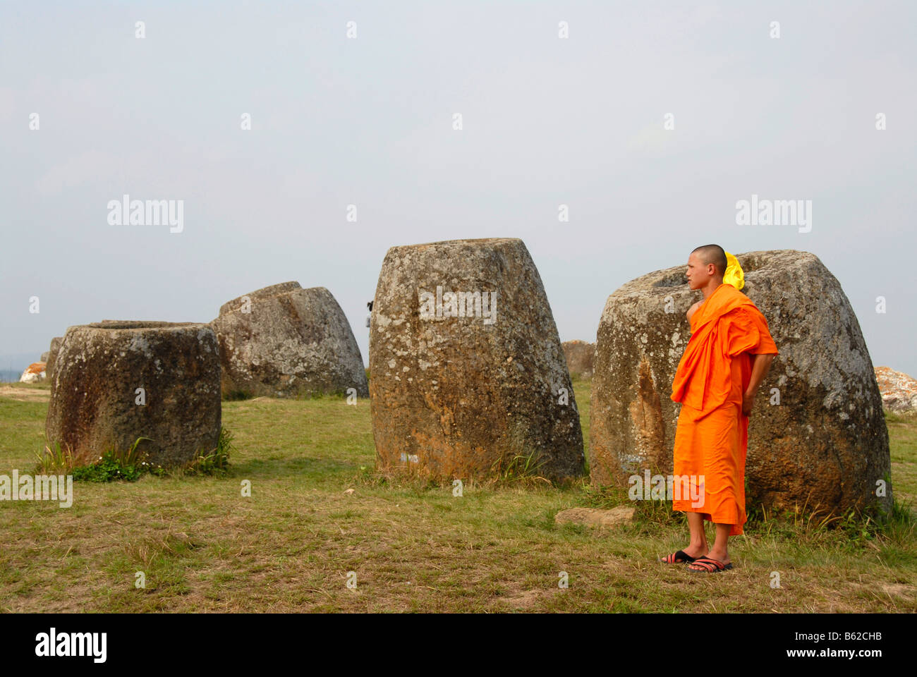 Junger Mönch trägt eine orangefarbene Kutte stehen vor enormen Gläser, Monolithen gemacht aus Stein, Plain of Jars Xieng Khuang Prov Stockfoto