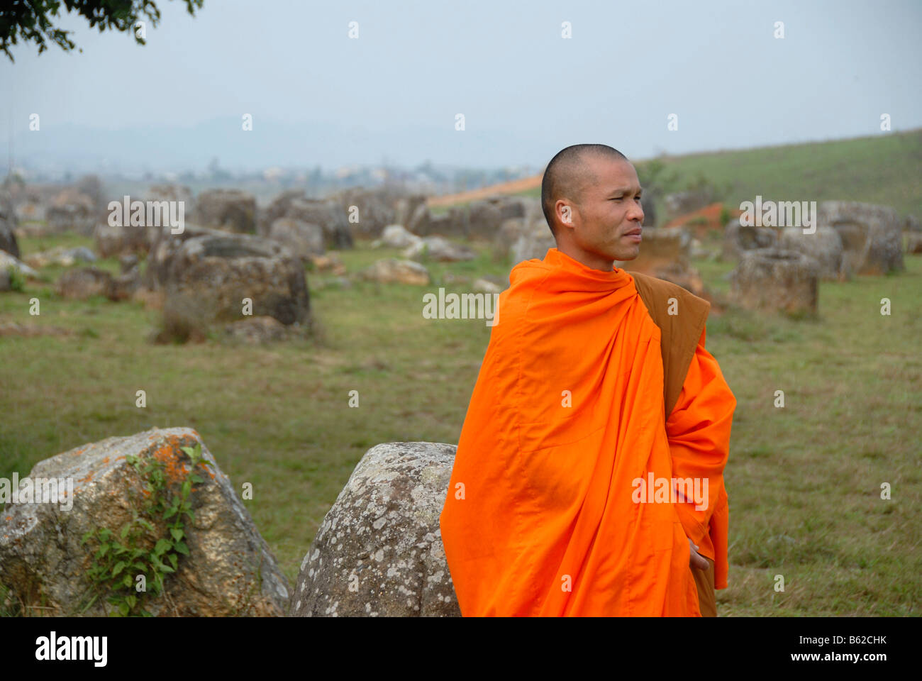 Junger Mönch trägt eine orangefarbene Kutte stehen vor enormen Gläser, Monolithen gemacht aus Stein, Plain of Jars Xieng Khuang Prov Stockfoto