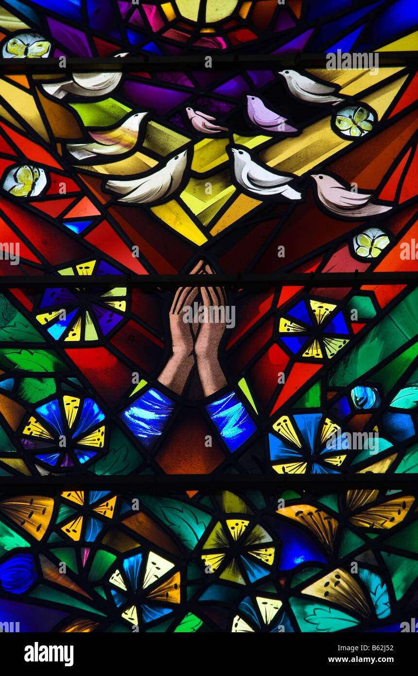 Ein Glasfenster mit betenden Händen und Tauben Stockfoto