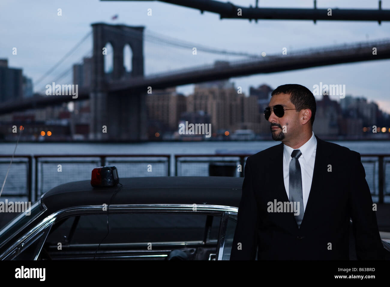 Ein Detektiv mit Sonnenbrille stützt sich auf ein Cougar 1967 unter der Brooklyn Bridge mit einer Sirene Licht auf dem Dach. Stockfoto