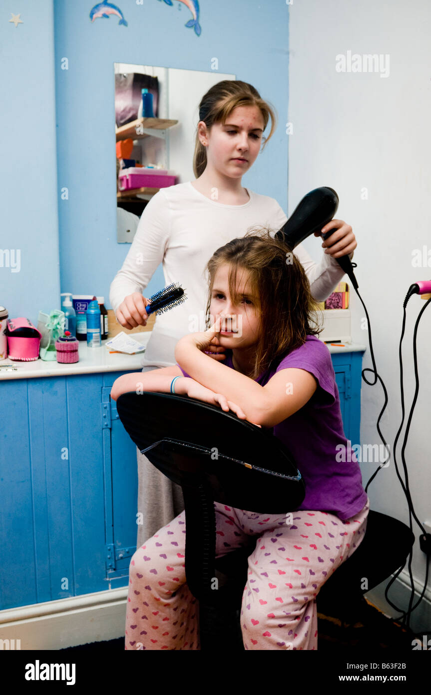 Teenager-Mädchen trocknen Haare zehn Jahre alten Schwestern mit einem elektrischen Fön in ihrem Schlafzimmer, UK Stockfoto