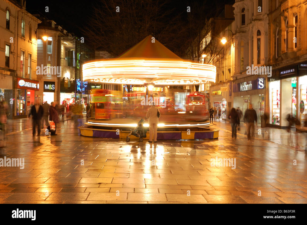 Nacht Schuss von Cardiff Queenstreet Geschäfte und Shopper A Oma wartet ein Kind auf dem drehenden Karussell Stockfoto