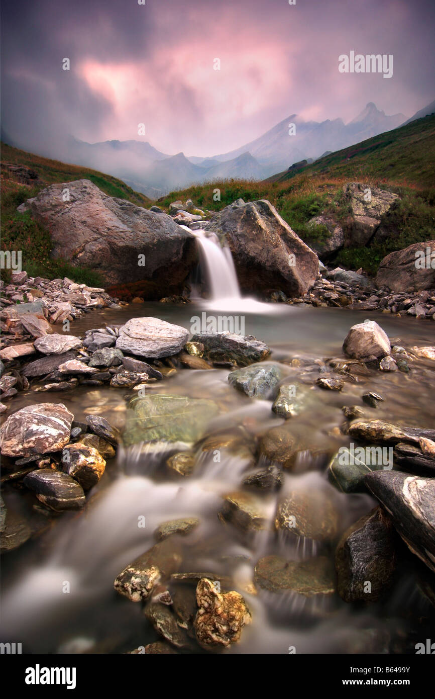 Ein kleiner Wasserfall in den italienischen Alpen, während eine schnelle bewegliche Front ins Tal Rollen war bei Sonnenuntergang aufgenommen. Stockfoto