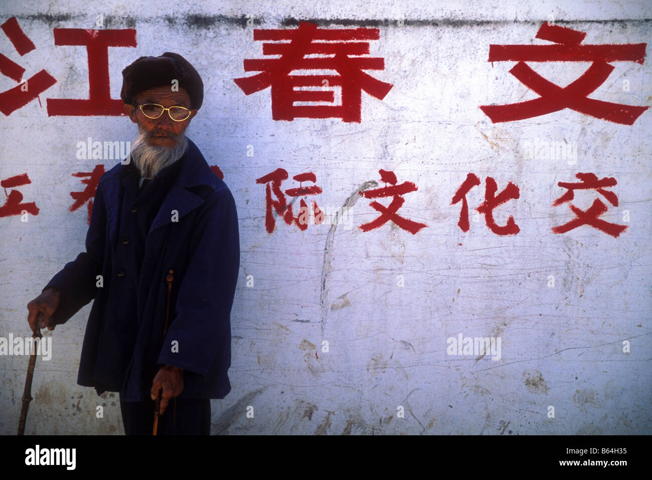 Alte chinesische Mann stand gegen die Wand mit chinesische Schrift Lijiang Yunnan Provinz China Stockfoto