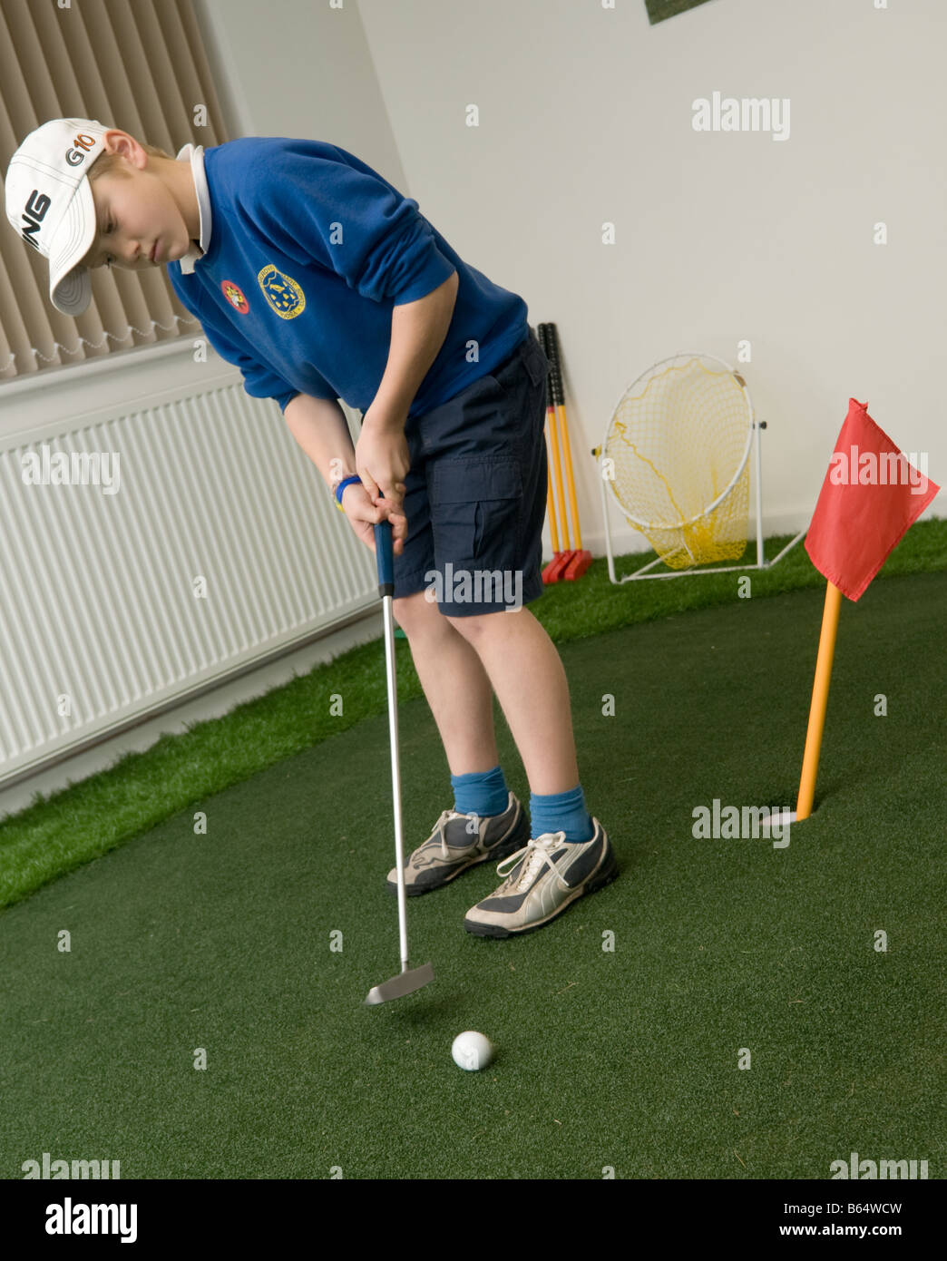 Ein kleiner Junge spielt Golf in Innenräumen gefährden Aberdyfi Golfclub Wales UK, üben seinem Schlaganfall auf Kunstrasen Stockfoto