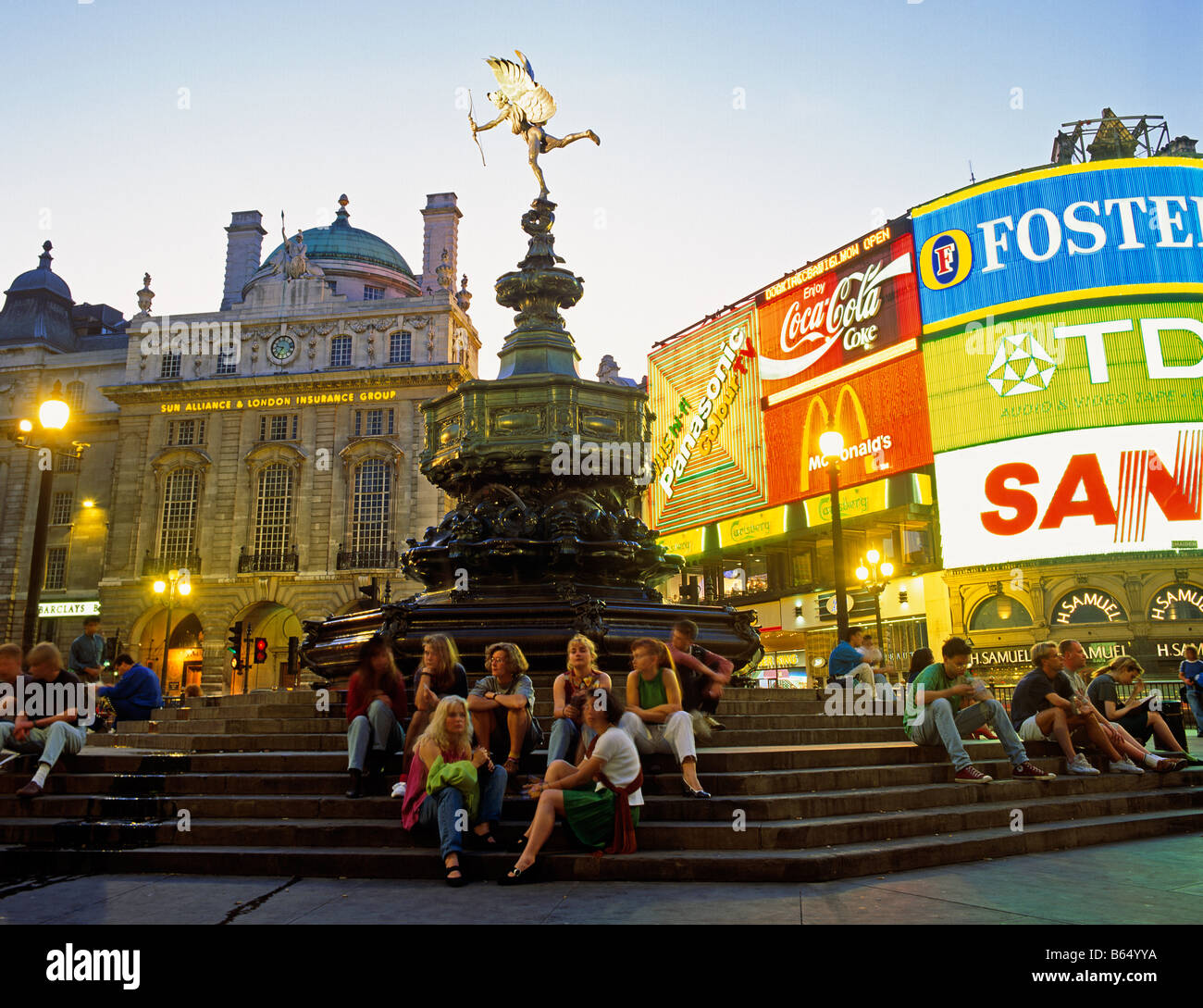 Touristen, die herumsitzen und Eros Piccadilly Circus West End London UK Europe Stockfoto