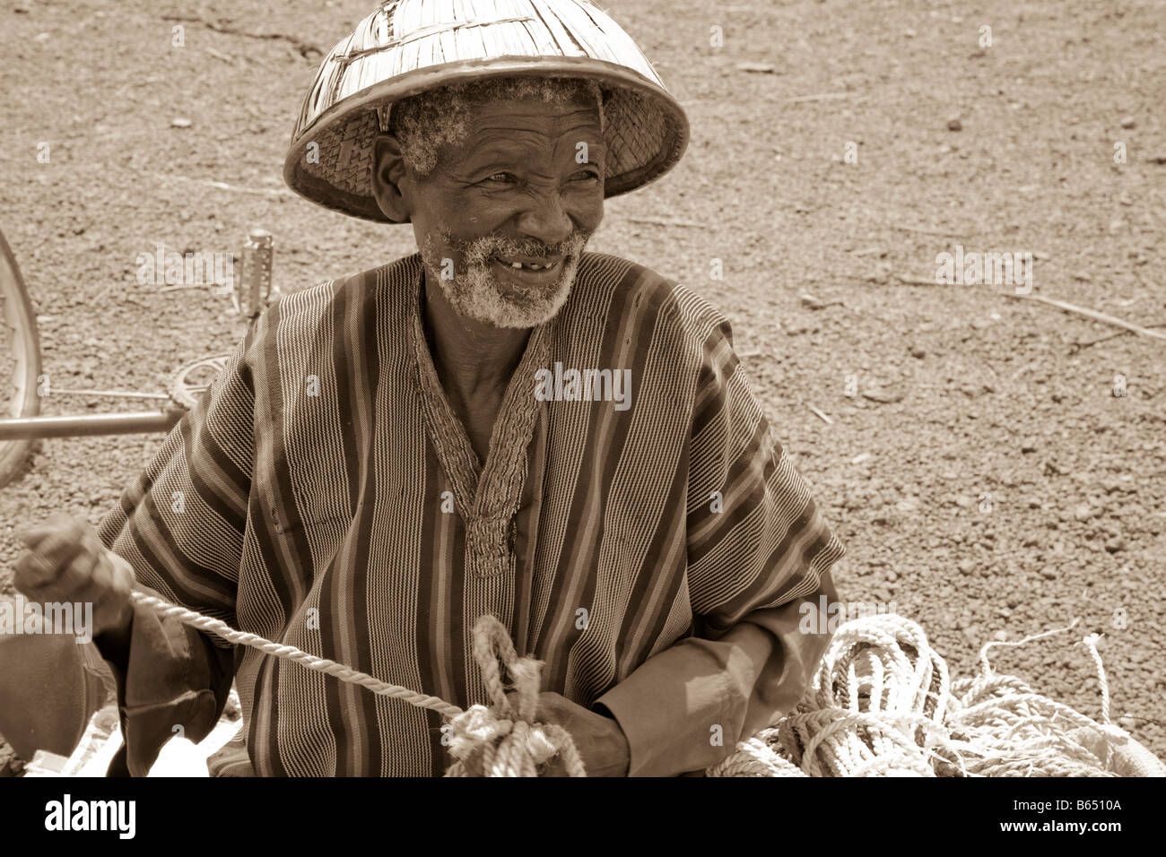 Ein Greis Fulani sitzt vor dem Tiermarkt in Kaya, Burkina Faso Weberei Seil, das er an die Marketgoers verkauft. Stockfoto