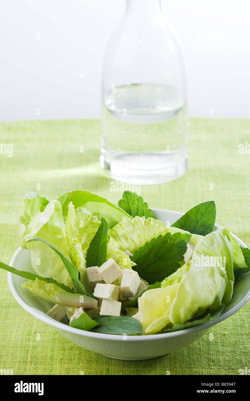 Salat von gemischten Grünen und Tofu Würfeln, Karaffe mit Wasser im Hintergrund Stockfoto