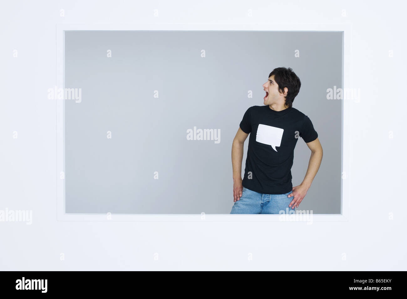 Junger Mann mit t-Shirt bedruckt mit leeren Wort Blase, Hände schreien, auf den Hüften Stockfoto