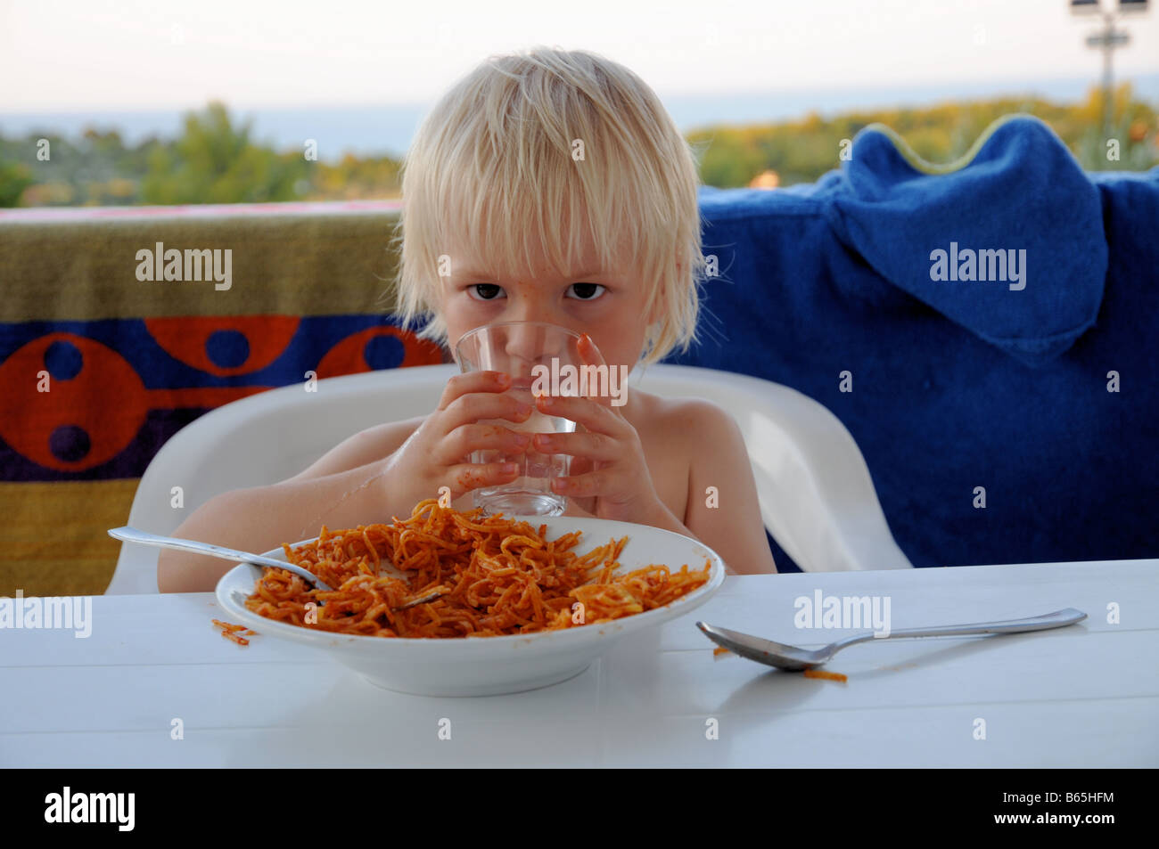 Ein kleiner Junge trinkt ein Glas Wasser beim Essen eines Teller Pasta während eines Urlaubs in Italien. Stockfoto